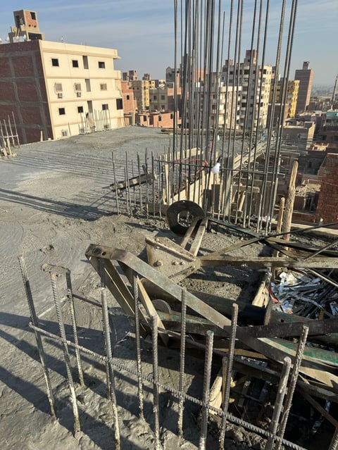 Construction site on urban rooftop with steel rebar framework, wooden forms, and city skyline in background