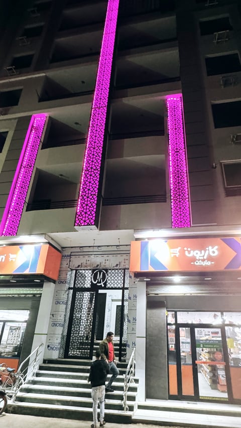 Modern building facade with bright pink neon vertical lights illuminating dark concrete structure and storefront entrance at night