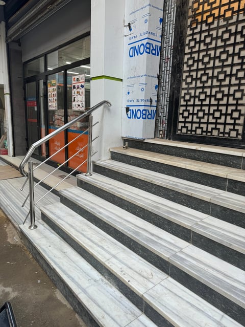 Storefront entrance with striped tile steps, metal handrail, and promotional signage indicating a shop opening or renovation