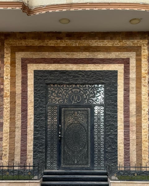 Ornate black metal doorway with decorative panels set within concentric rectangular stone frames of varying earth tones
